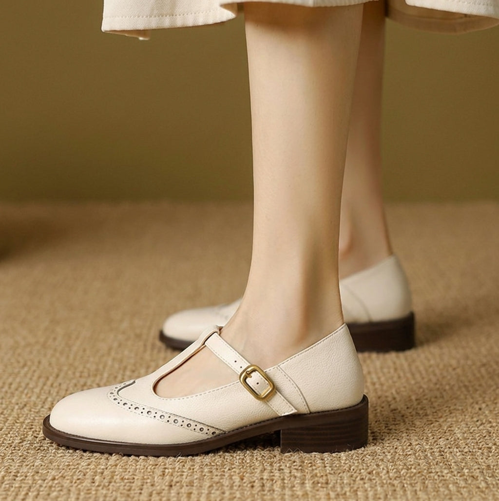 Cream women's Mary Jane brogue flats with low heels and buckle straps, side view on feet