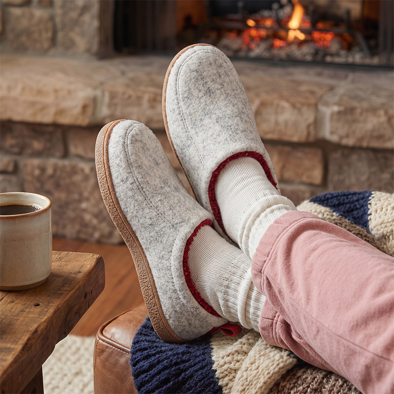 White fleece-lined house slippers worn with socks while relaxing beside a fireplace