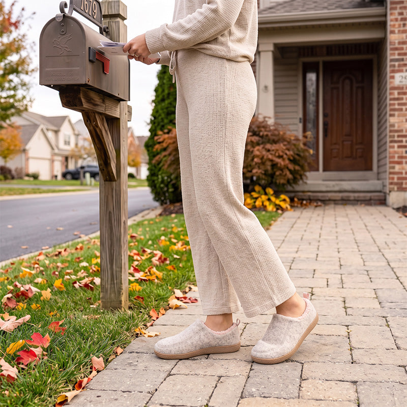 Pink fleece-lined house slippers worn on a paved path outside a home