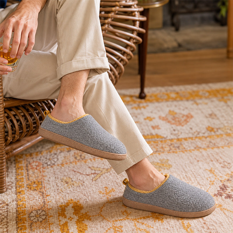 Grey house slippers with yellow lining, worn while sitting in a wicker chair