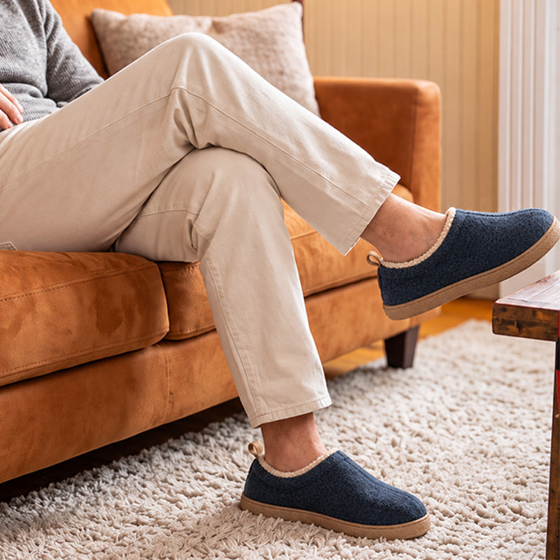 Navy fleece-lined house slippers worn while relaxing on a sofa