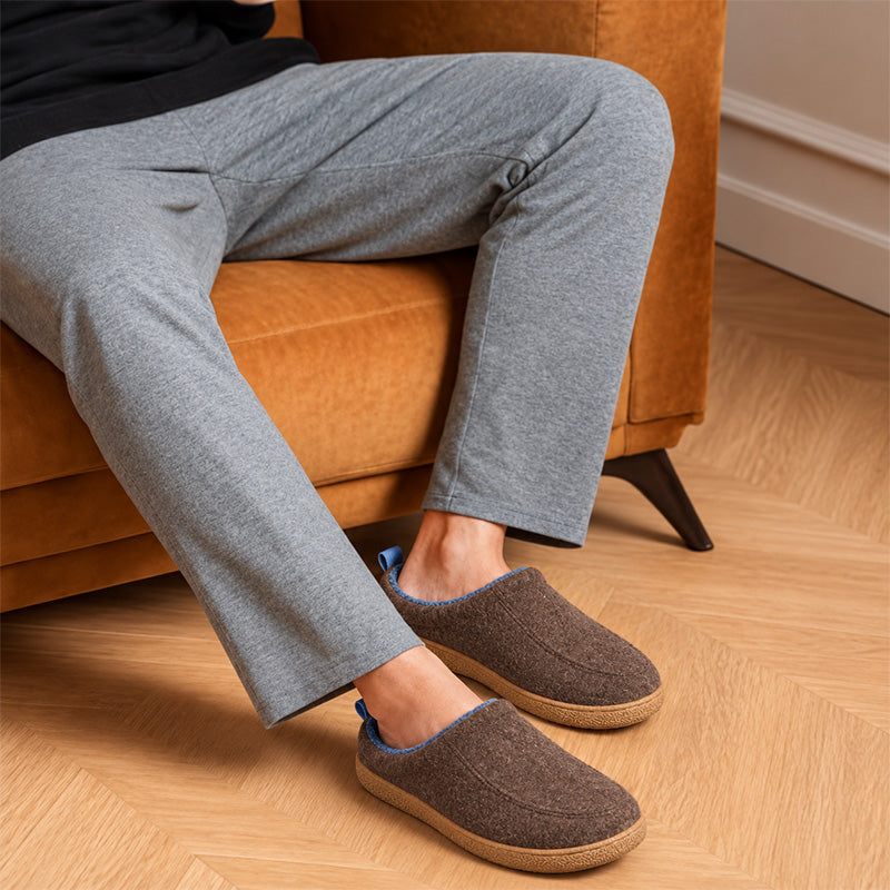 Brown house slippers with blue lining, worn while sitting on a sofa