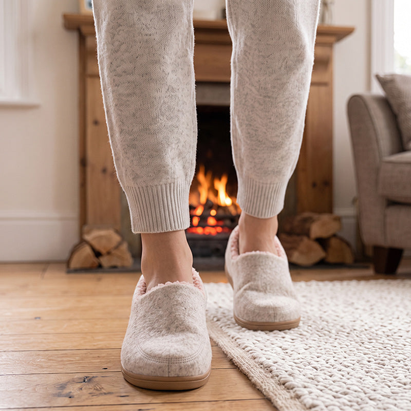 Pink fleece-lined house slippers worn in front of a fireplace, shown from the front