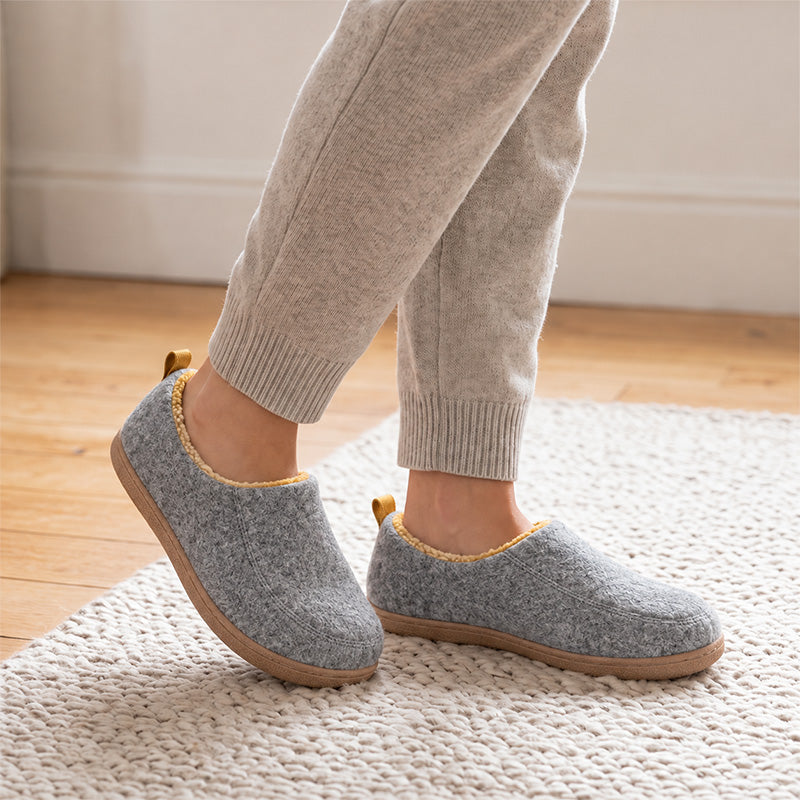 Grey house slippers with yellow lining, worn on a rug and shown at an angle