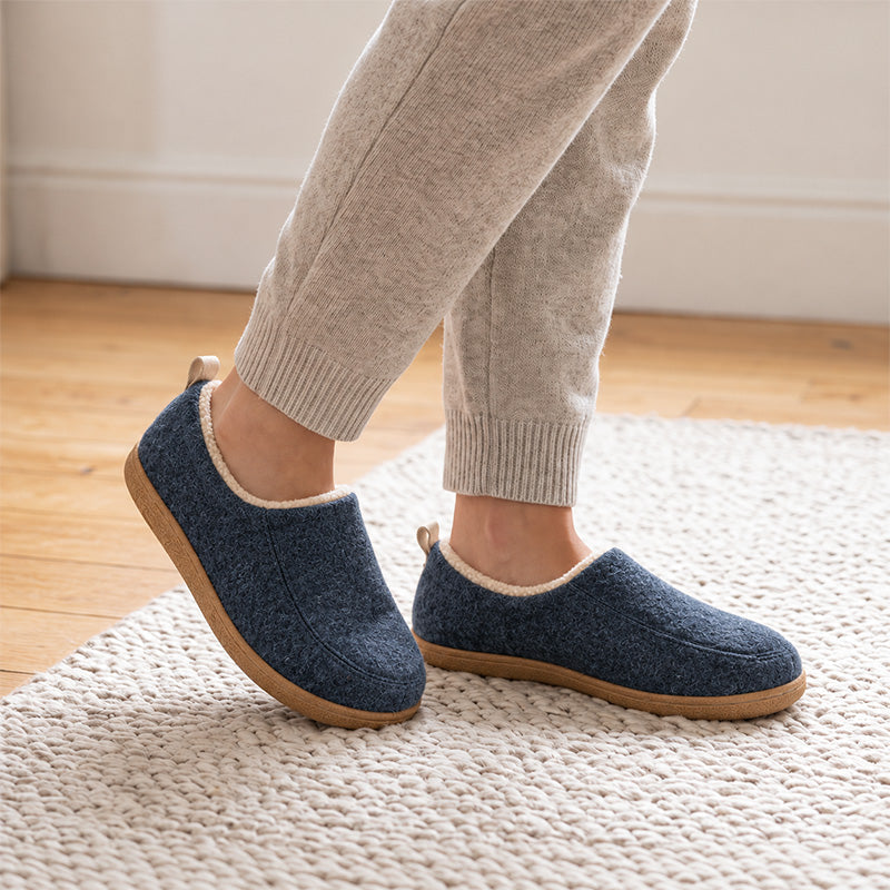Navy fleece-lined house slippers worn on a rug, shown from an angled side view