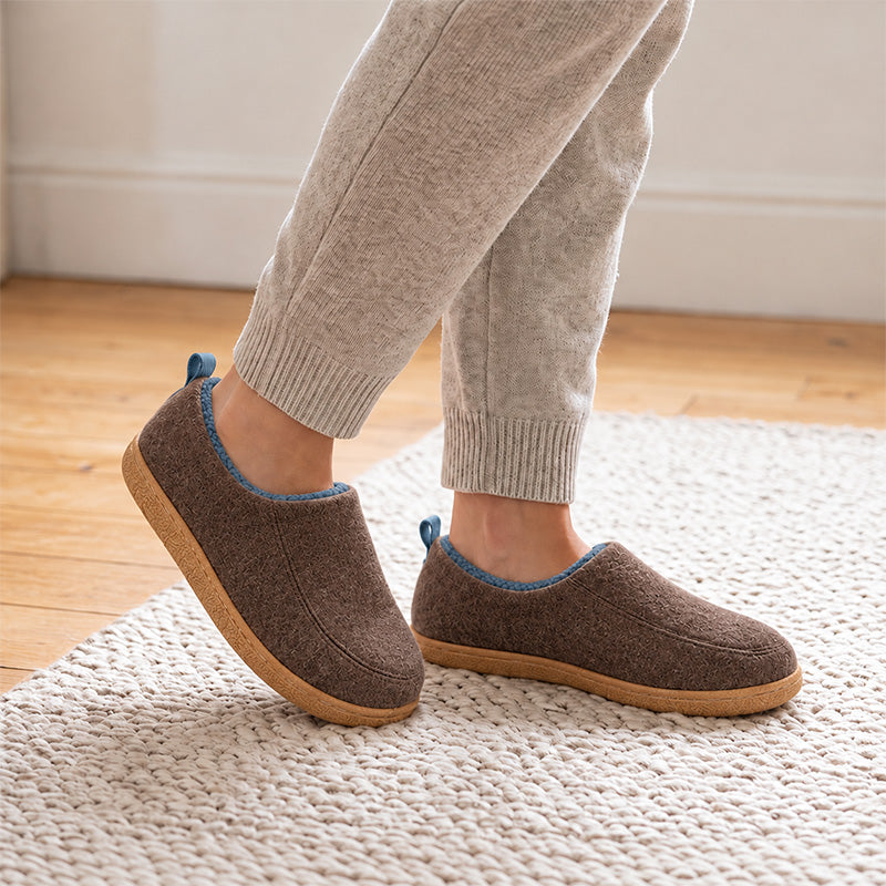Brown house slippers with blue lining, worn on a rug and shown at an angle