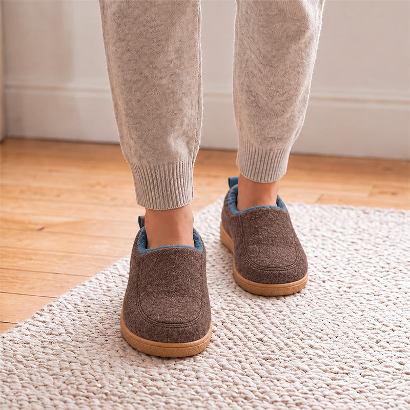 Brown house slippers with blue lining, shown from the front while worn