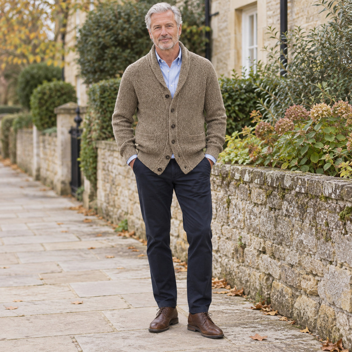 Mature adult man wearing the khaki textured shawl-collar cardigan over a light blue collared shirt with navy trousers on a stone walkway.