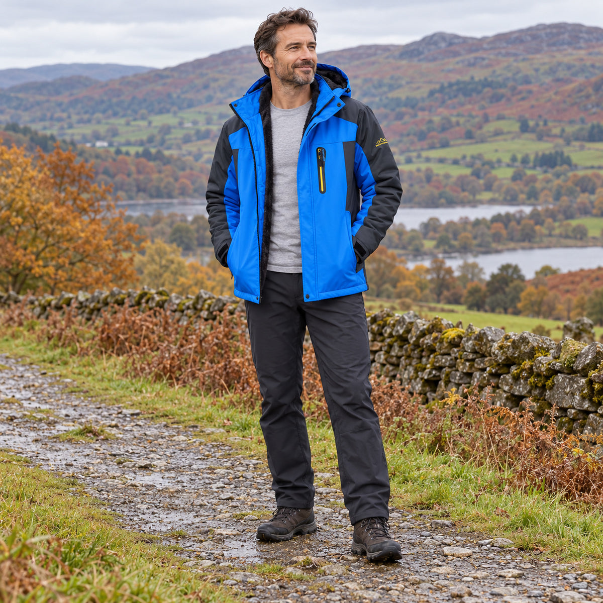 Man wearing the open blue padded jacket over a grey top on a countryside path, shown from head to both walking boots