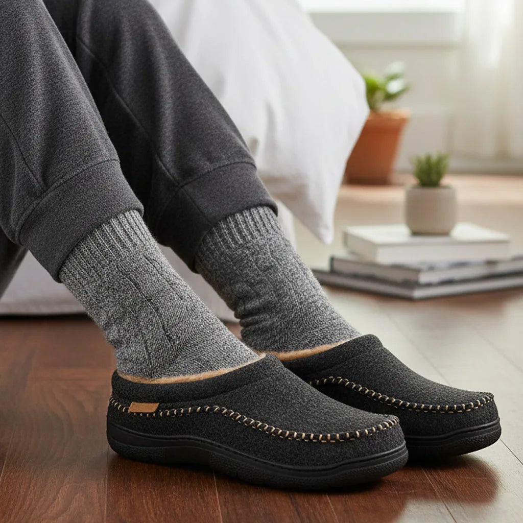Black fleece-lined moccasin slippers worn with grey socks indoors