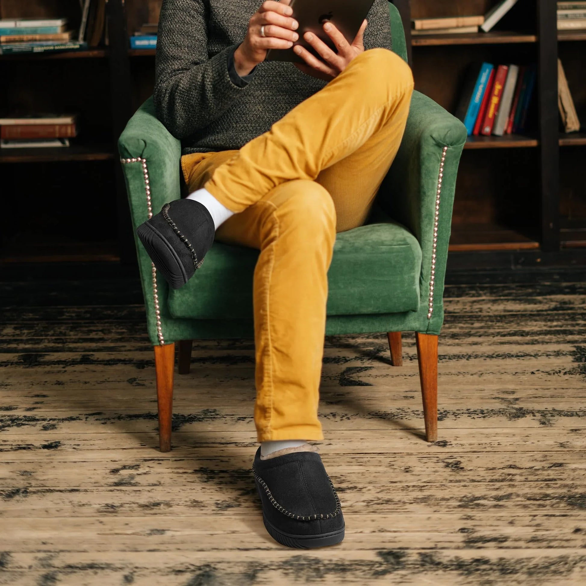 Black moccasin house slippers worn with mustard trousers while reading