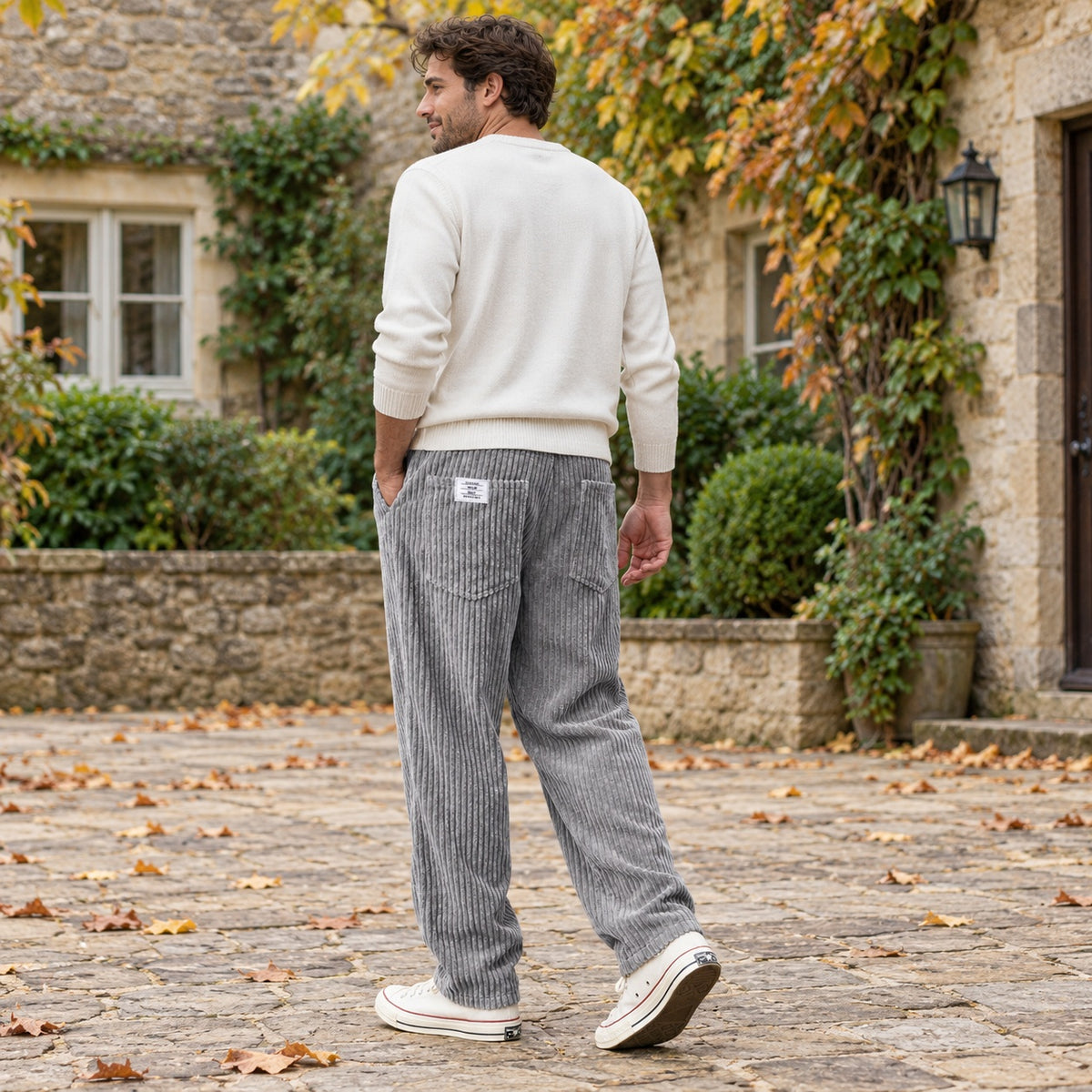 Man wearing the grey ribbed trousers with trainers in a relaxed outdoor setting, shown from head to both shoes
