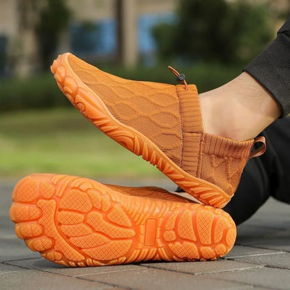 Brown barefoot-style slip-on shoe worn on foot with broad rounded forefoot and outsole visible