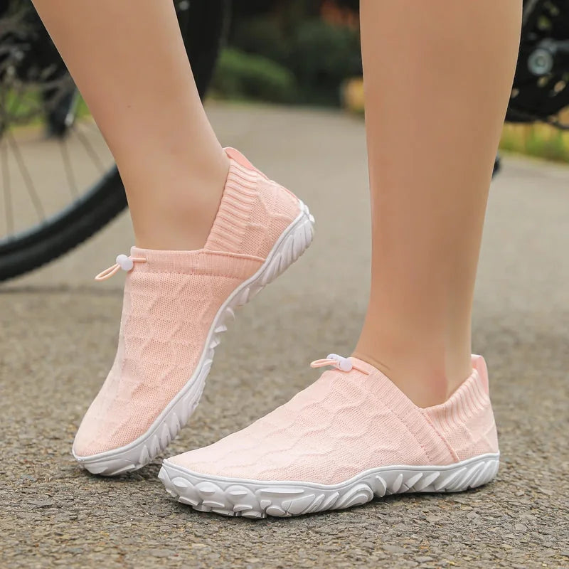 Pink barefoot-style slip-on shoes worn outdoors with a broad rounded toe shape