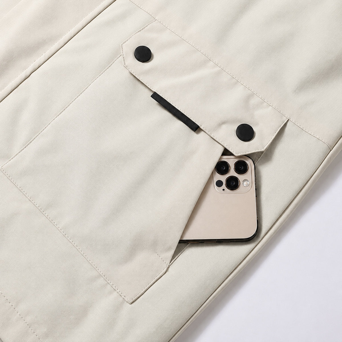 Stone jacket lower pocket with two black press studs and a side-entry opening holding a phone.