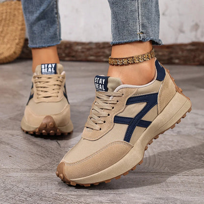 Women's beige and navy walking trainers worn from a front three-quarter view