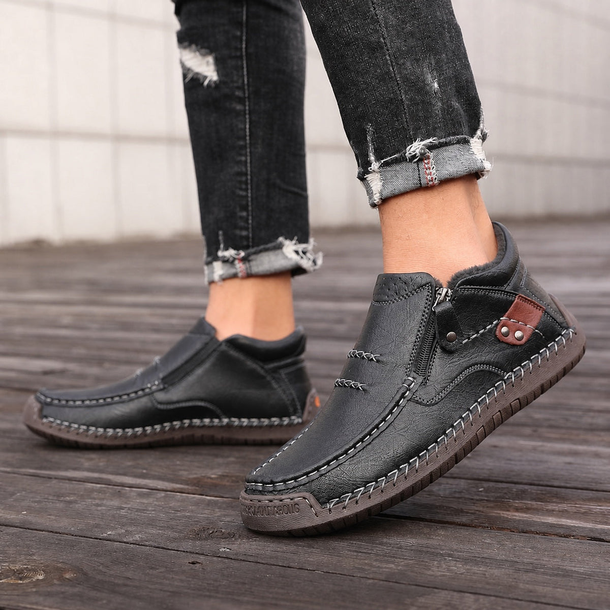 Black men's zip-up leather ankle boots with stitched soles, worn with jeans