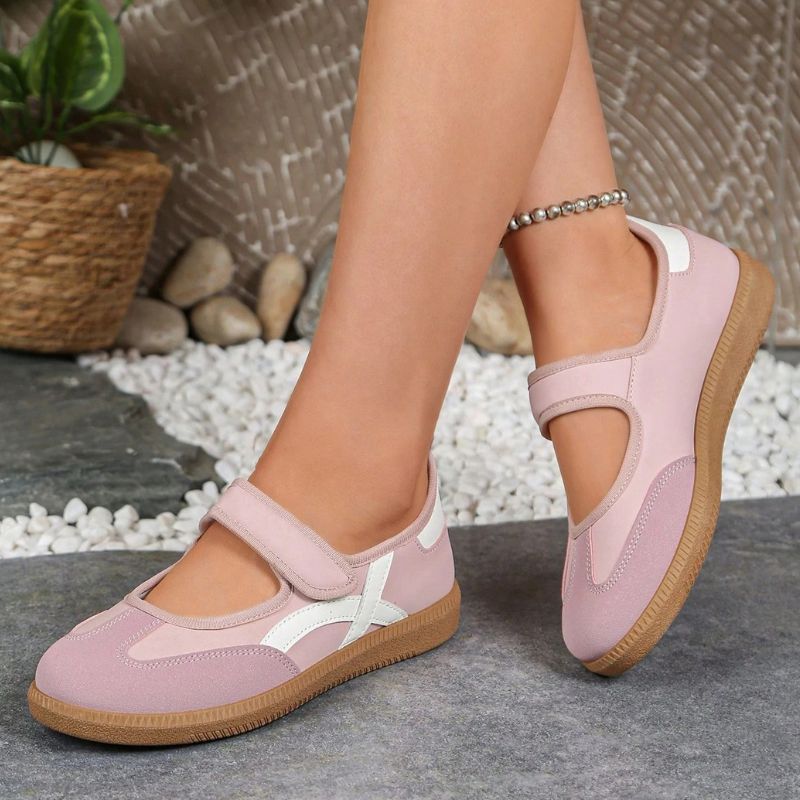 Pink and white women's Mary Jane trainers with adjustable straps, angled view on feet