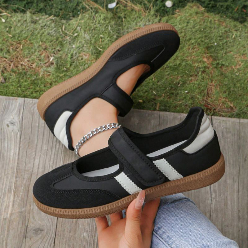 Black women's Mary Jane trainers with white stripes, showing the strap and gum sole