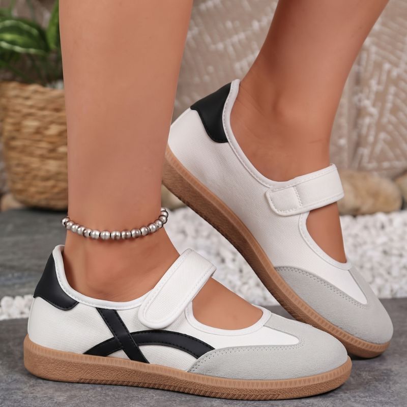 White women's Mary Jane trainers with black curved stripes, side view on feet