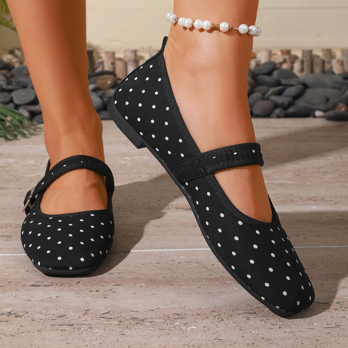 Black polka-dot women's Mary Jane flats with adjustable straps, front close-up on feet