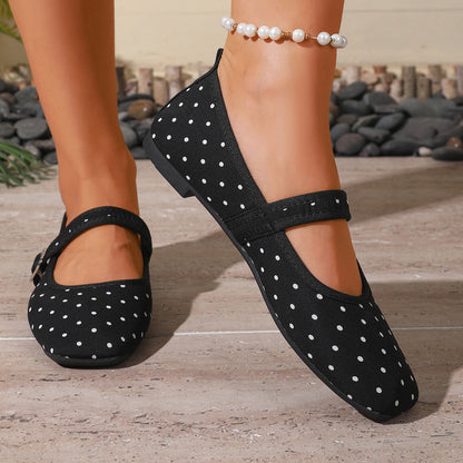 Black polka-dot women's Mary Jane flats with adjustable straps, front close-up on feet