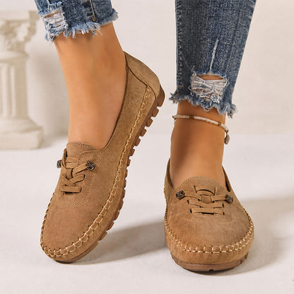 Tan women's suede slip-on loafers with stitched edges, front view on feet