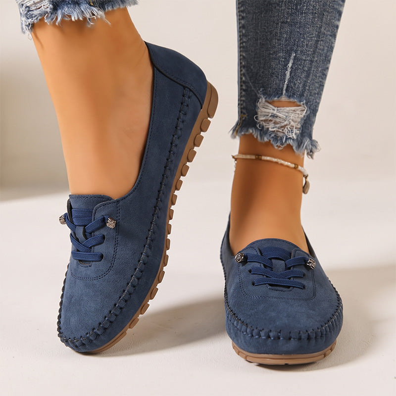 Navy women's suede slip-on loafers with stitched edges, front view on feet