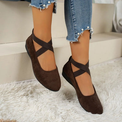 Brown cross-strap flats for women, worn indoors on a light rug