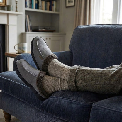 Auldweave Men’s warm wide fit winter slippers. Person wearing slippers and socks on a blue couch in a cozy living room.
