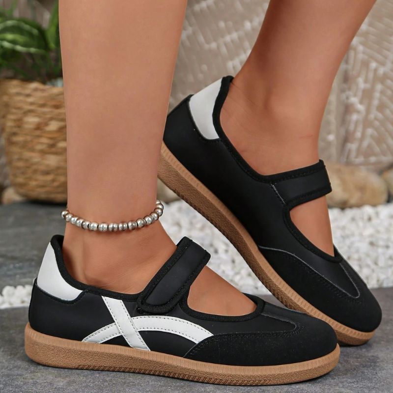 Black and white women's Mary Jane trainers with adjustable straps, side view on feet
