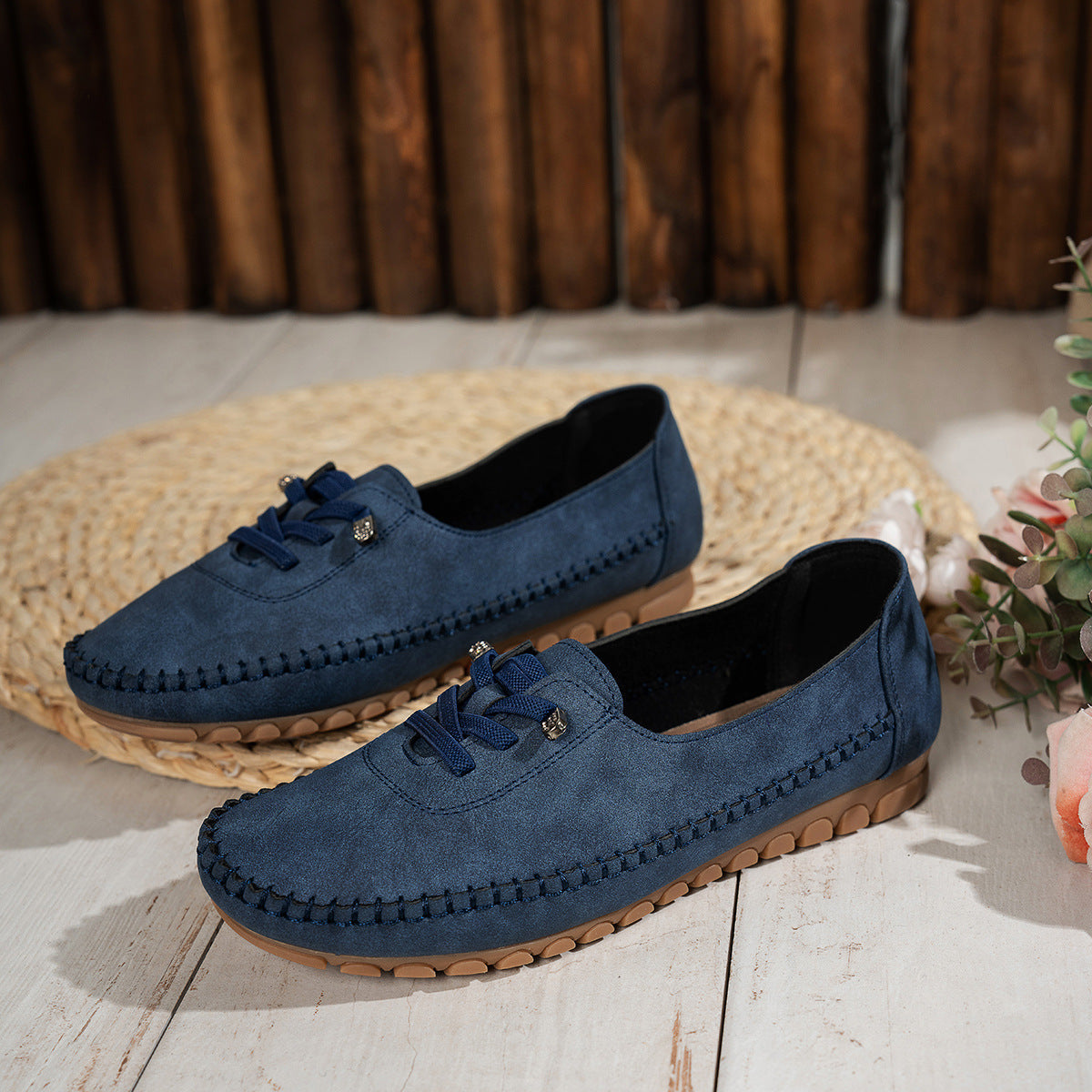 Navy women's suede loafers with stitched edges, pair displayed beside flowers