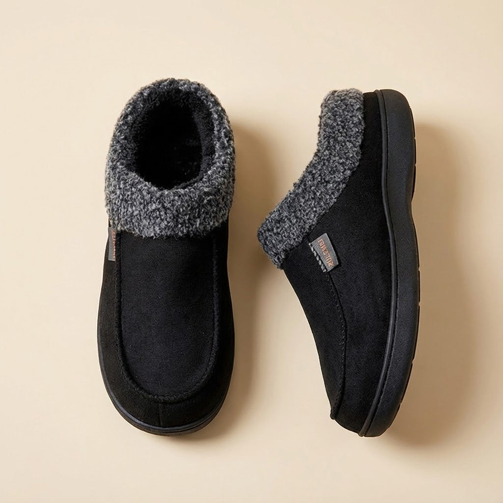 Auldweave Men’s warm wide fit winter slippers. Pair of black slippers with fuzzy trim on a beige background
