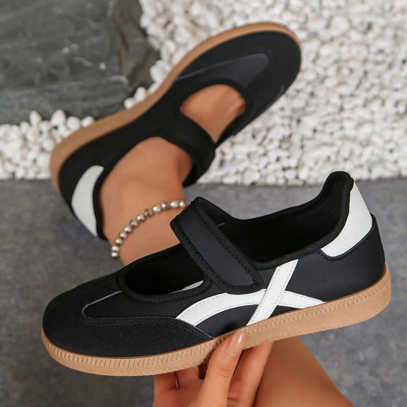 Black women's Mary Jane trainers with white curved stripes, showing the strap and gum sole