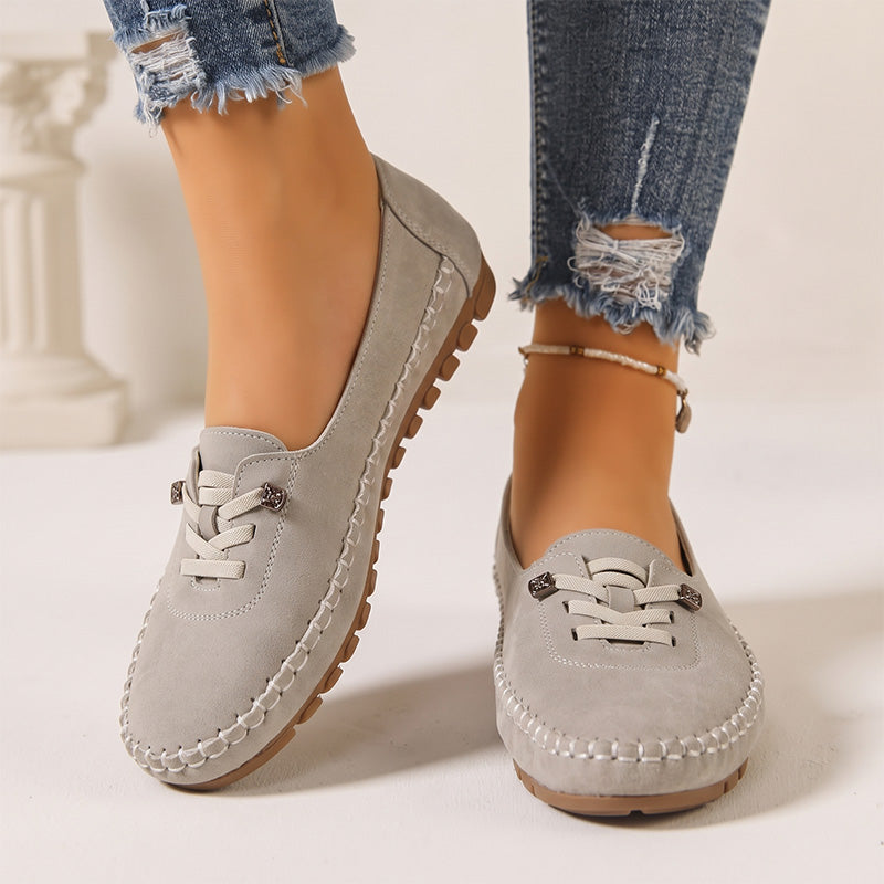 Light grey women's suede slip-on loafers with stitched edges, front view on feet