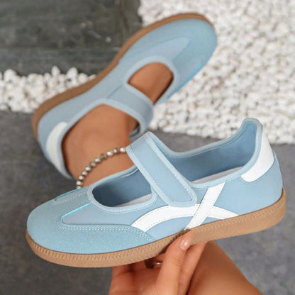 Blue women's Mary Jane trainers with white curved stripes, showing the strap and gum sole