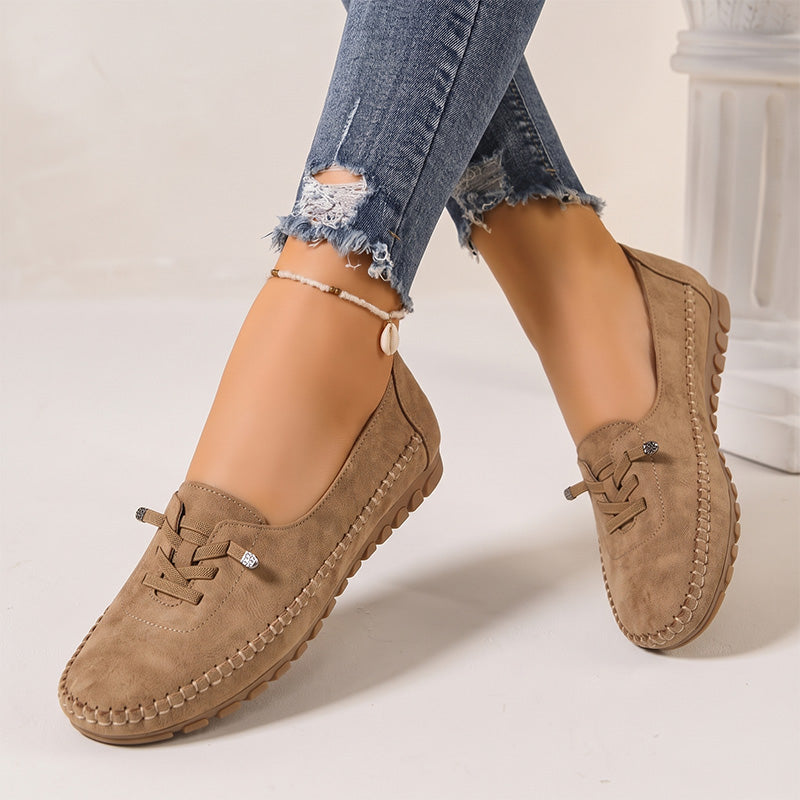 Tan women's suede slip-on loafers with rounded toes, angled view on feet