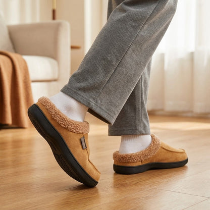 Auldweave Men’s warm wide fit winter slippers. Person wearing brown slippers on a wooden floor with a blurred background