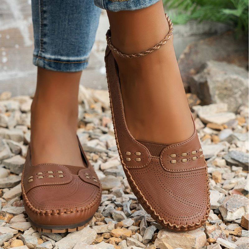 Tan women's perforated leather loafers with stitched edges, front view on feet