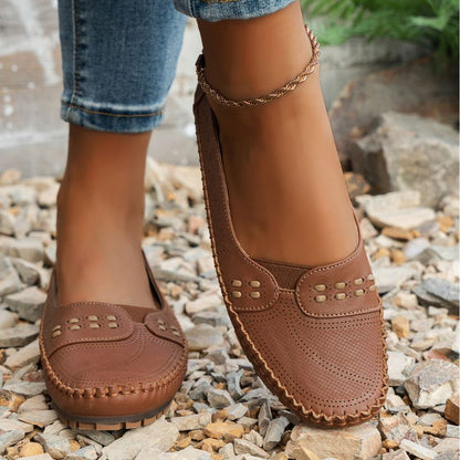Tan women's perforated leather loafers with stitched edges, front view on feet
