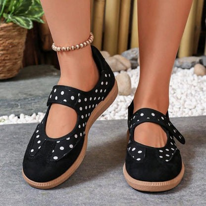 Black polka-dot women's Mary Jane trainers with broad straps, front view on feet