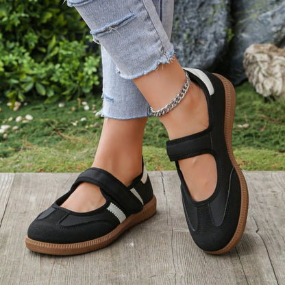 Black women's Mary Jane trainers with white side stripes, angled view on feet