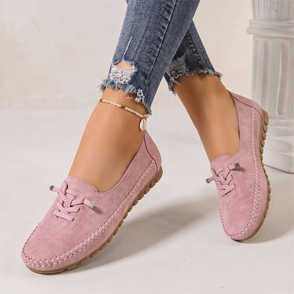 Pink women's suede slip-on loafers with rounded toes, angled view on feet