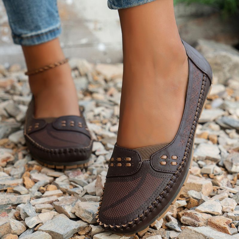 Dark brown women's leather loafers with decorative cut-outs, angled view on feet