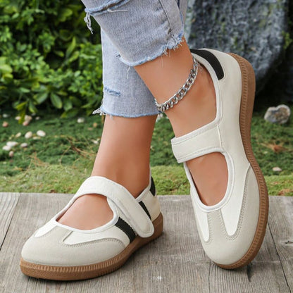 Cream and black women's Mary Jane trainers with adjustable straps, angled view on feet