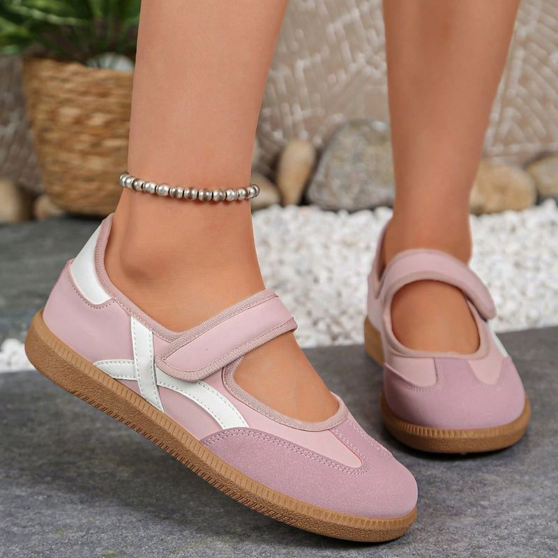 Pink women's Mary Jane trainers with white curved stripes, side view on feet