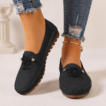 Black women's suede slip-on loafers with stitched edges, front view on feet