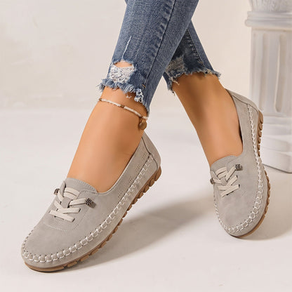 Light grey women's suede slip-on loafers with rounded toes, angled view on feet
