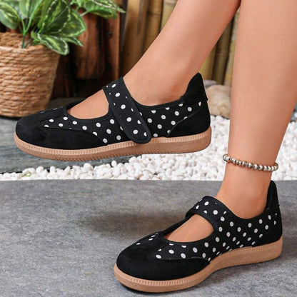 Black polka-dot women's Mary Jane trainers showing the strap fastening on feet