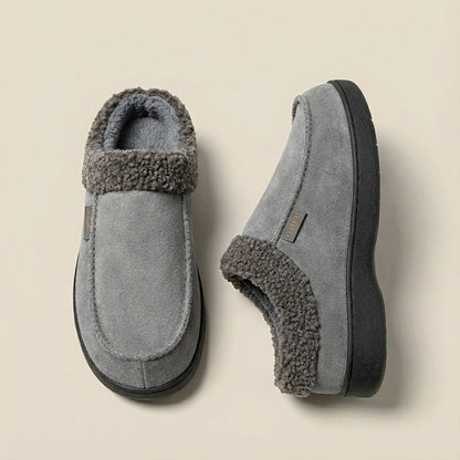 Auldweave Men’s warm wide fit winter slippers. Pair of grey slippers with fuzzy trim on a beige background